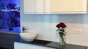 A modern bathroom with a white sink, a black countertop, and a vase with a red rose.