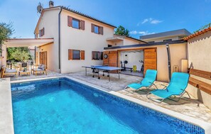 A poolside area with a table tennis table, lounge chairs, and a covered seating area.