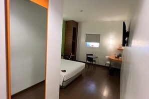 Ein Hotelzimmer mit Bett, kleinem Schreibtisch, Stuhl und Fenster.