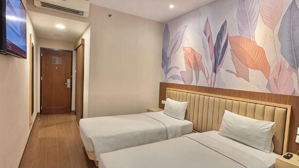 A hotel room with two beds, a wooden headboard, a TV, and a wall with a leaf pattern. - Alltrue Lite Hotel Nagoya Hill Batam (Nagoya)