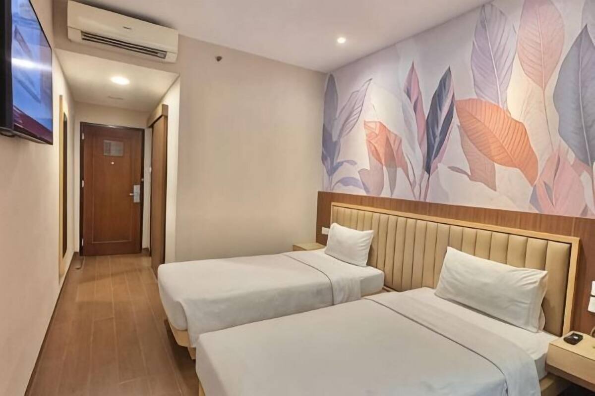 A hotel room with two beds, a wooden headboard, a TV, and a wall with a leaf pattern.