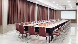 A conference room with a long table, chairs, a projector screen, and curtains. - Alltrue Lite Hotel Nagoya Hill Batam (Nagoya)