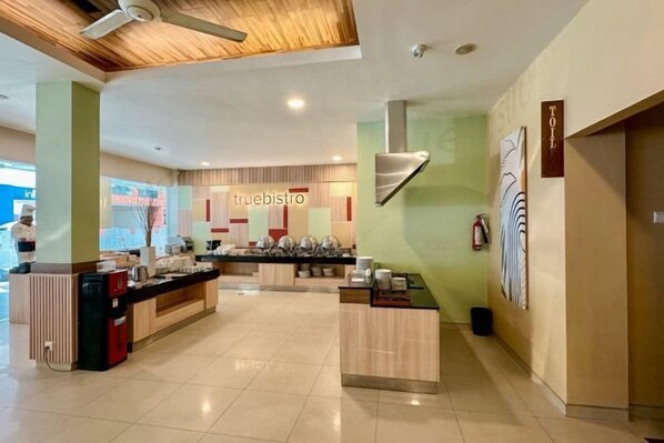 A hotel lobby with a reception desk, a coffee station, and a sign for the restaurant.