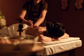 Een massage in een kamer met weinig licht, met een massagetafel en iemand die een rugmassage ontvangt.