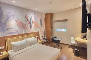 Ein Hotelzimmer mit einem Bett, einem Schreibtisch, einem Sessel, einem kleinen Tisch und einem an der Wand befestigten Fernseher.