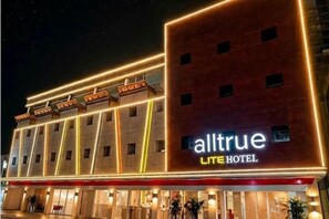 Een hotel met een moderne gevel, meerdere balkons en een opvallend bord met de tekst 'alltrue Lite Hotel'.