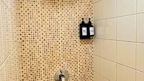 Un mur recouvert de carreaux, avec un panneau de commande pour la douche et un robinet.