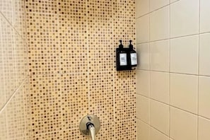 Un mur recouvert de carreaux, avec un panneau de commande pour la douche et un robinet.