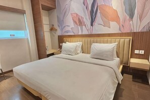 A large bed with a wooden headboard, two bedside tables, and a wall with a floral pattern. - Alltrue Lite Hotel Nagoya Hill Batam (Nagoya)