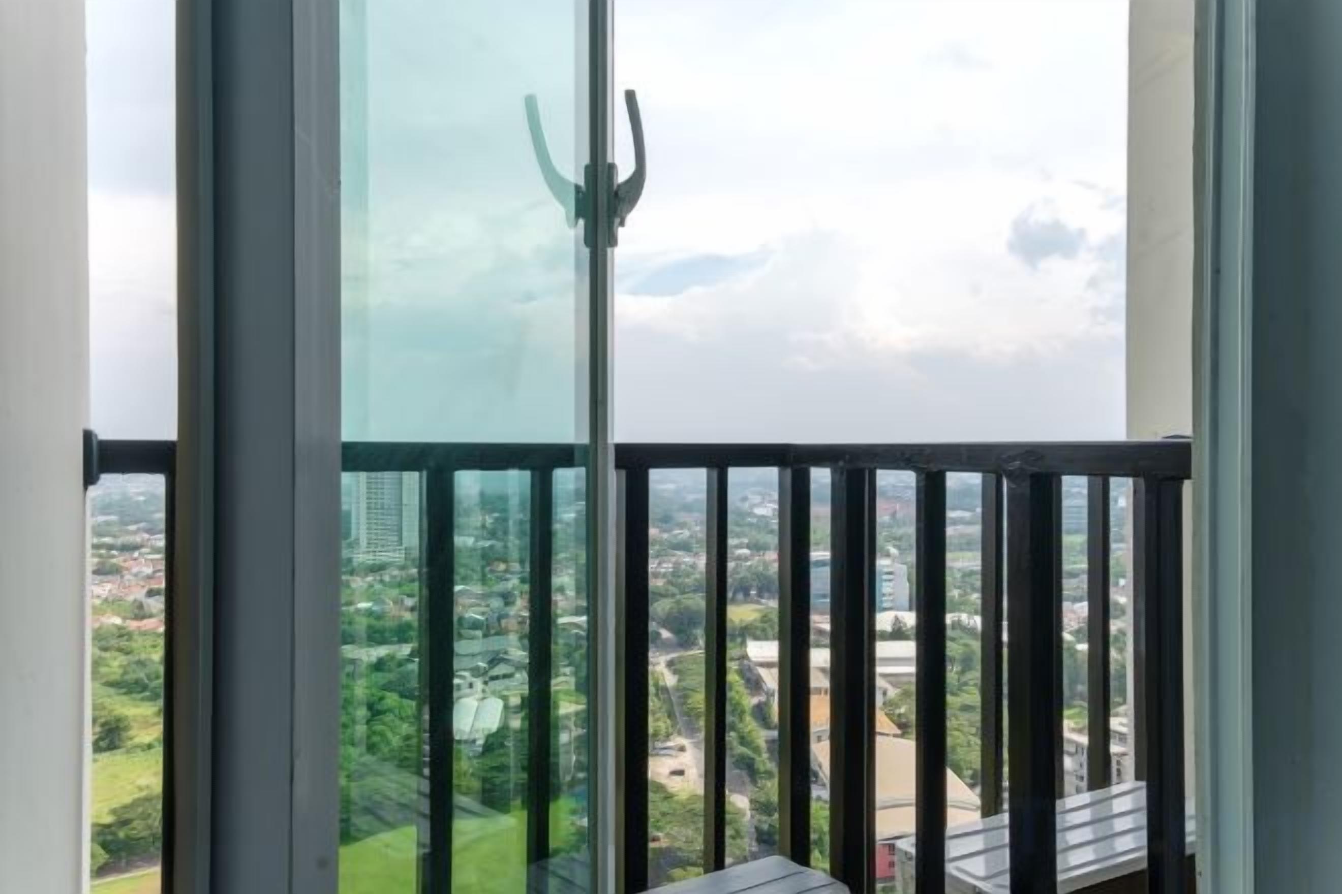 A balcony with a glass door, offering a view of a cityscape with buildings and greenery.