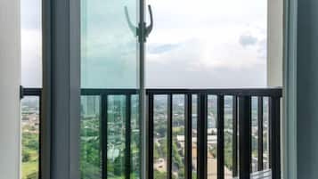 A balcony with a glass door, offering a view of a cityscape with buildings and greenery.