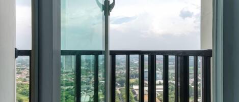A balcony with a glass door, offering a view of a cityscape with buildings and greenery.