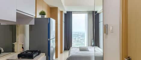 A compact hotel room with a kitchenette, a bed, and a view of the city.