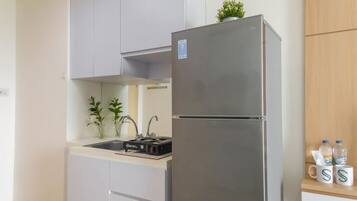 A compact kitchen with a stainless steel refrigerator, a sink, and a small countertop with a coffee machine and two potted plants.