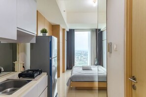A modern hotel room with a kitchenette, a bed, and a view of the city. - Gala by TwoSpaces Studio @TreePark Apartment (Serpong)