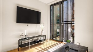 Una sala de estar moderna con un televisor de pantalla plana grande montado en la pared, una consola negra con un jarrón y velas, y un suelo de madera con un tapete estampado.