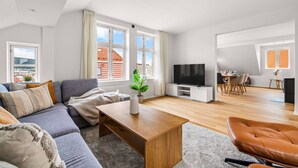 Een moderne woonkamer met een bank, salontafel, televisie, eethoek en grote ramen.