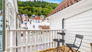 Een balkon met een houten vloer, een witte leuning en twee zwarte stoelen.