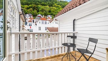 Un balcone con pavimento in legno, ringhiera bianca e due sedie nere.