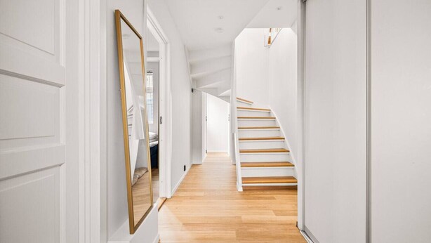 Een moderne hal met witte wanden, houten vloer en een trap met witte leuningen.