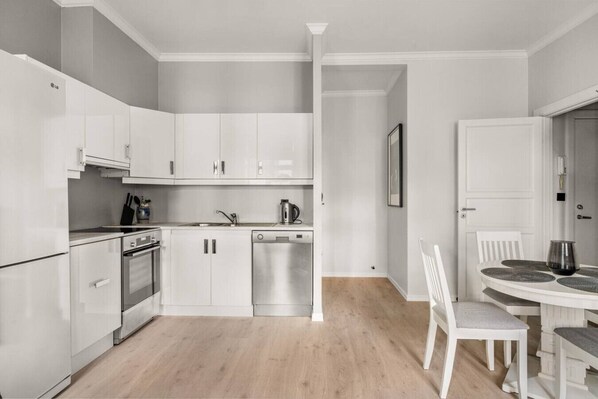 A modern kitchen with white cabinetry, a dishwasher, and a dining area with a white table and chairs.