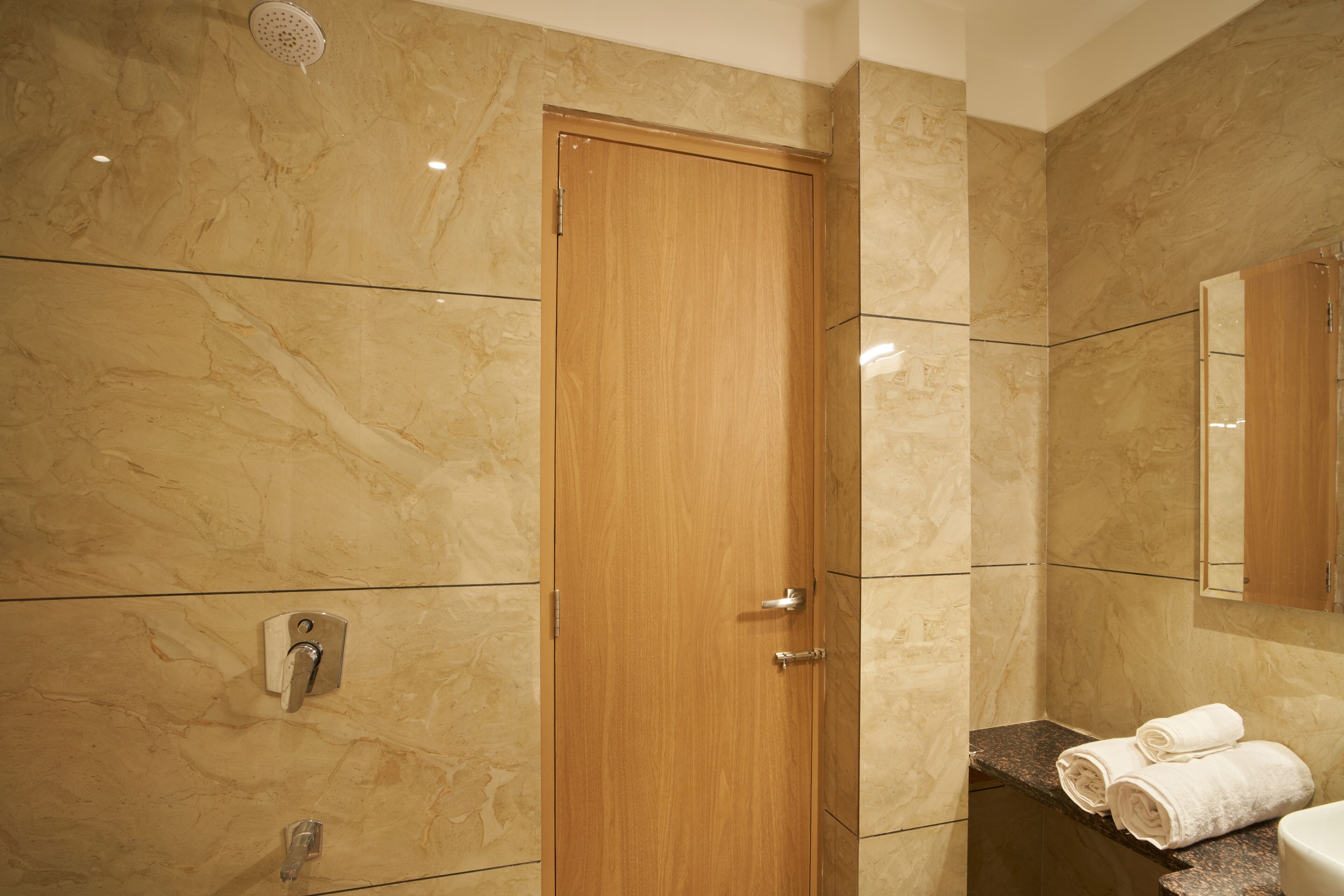 A bathroom with a wooden door, marble walls, a sink with a granite countertop, and a mirror above the sink.