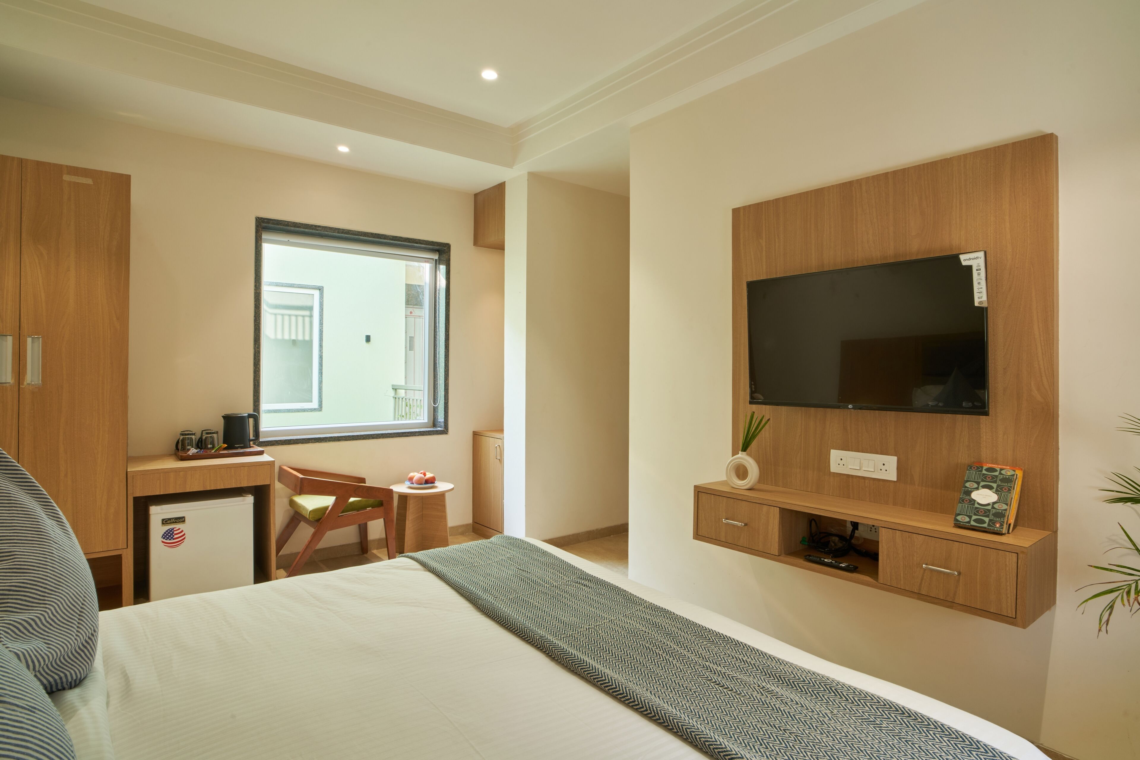 Hotelkamer met een bed, een bureau met stoel, een aan de muur bevestigde televisie en een kleine koelkast.