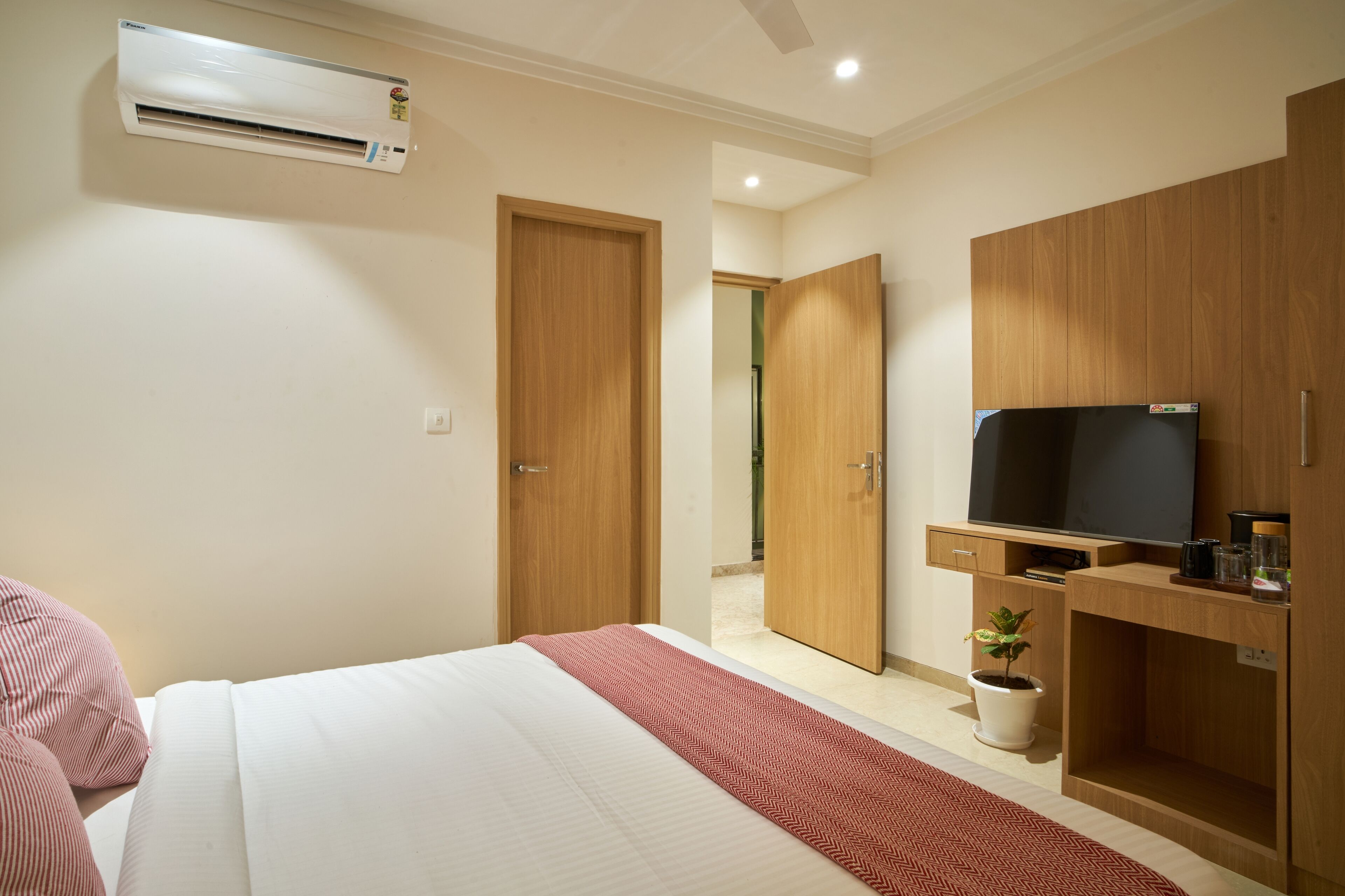 A hotel room with a bed, a TV, a potted plant, and wooden furniture.
