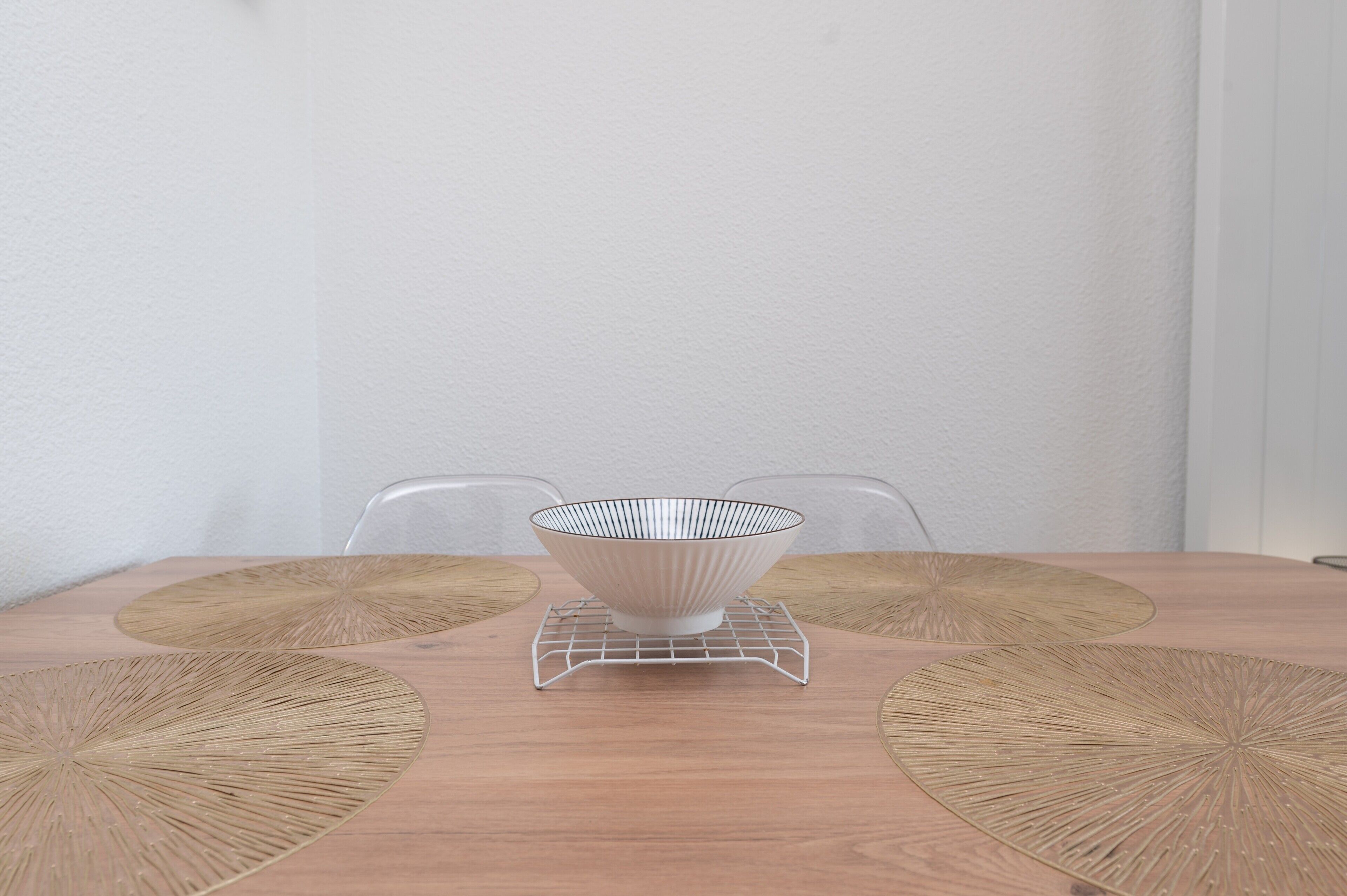 Een eettafel met een witte kom op een metalen onderzetter, omringd door twee gevlochten placemats.