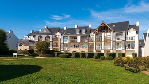 A multi-story residential building with balconies, a lawn, and a bench. - Studio L'Océanic, summer pool, near beach and port, parking, towels & cleaning extra (Arzon)