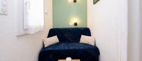 A small room with a dark blue sofa, two white pillows, a wooden table with a candle, and a green accent wall.