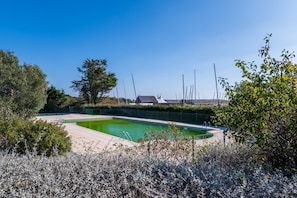 Une piscine entourée d’une terrasse, avec une clôture et un bâtiment en arrière-plan.