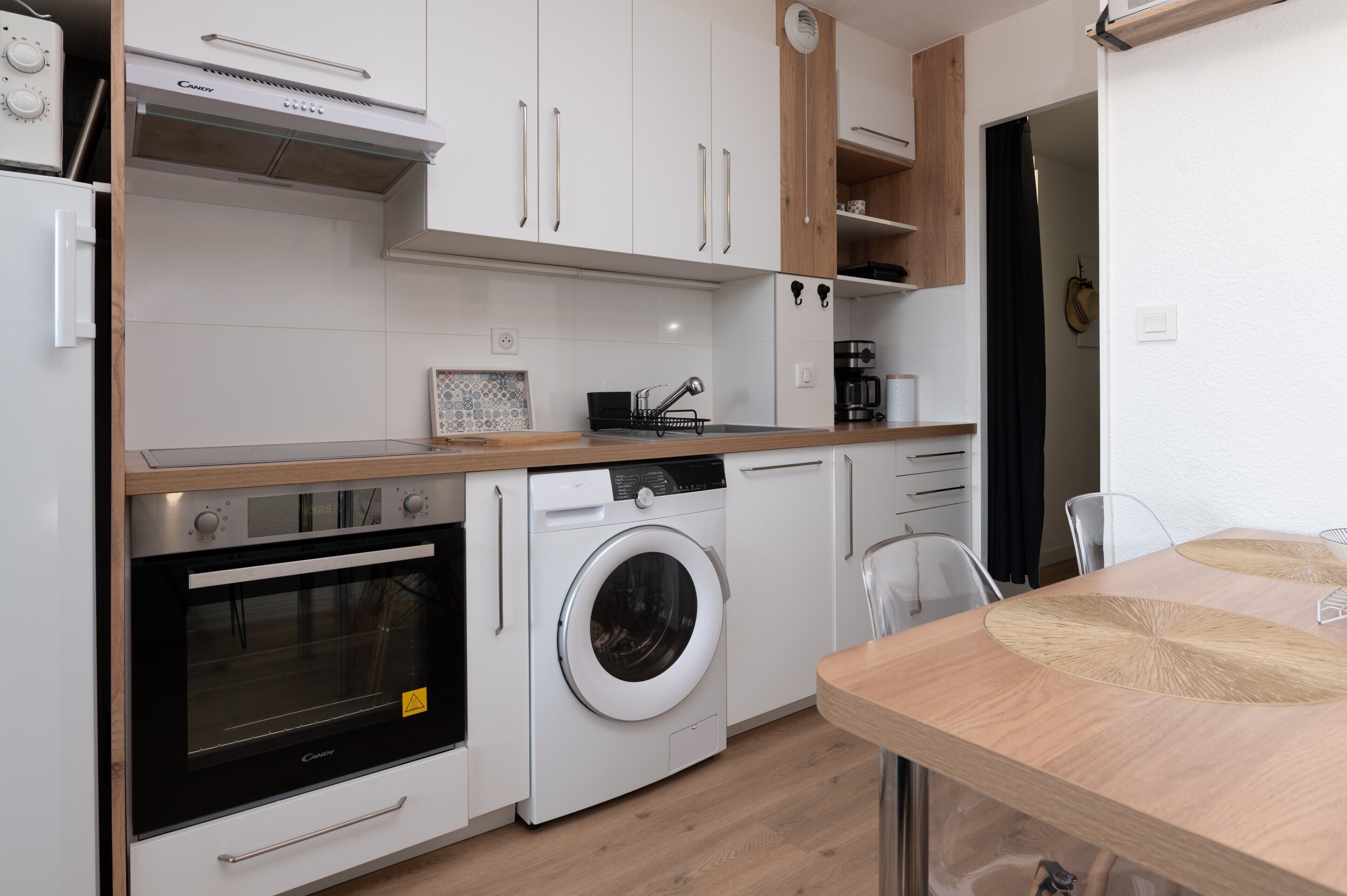 A compact kitchen with a built-in oven, a washing machine, and a coffee maker.