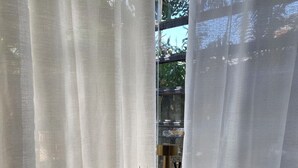 A small round table with a white chair in front of a window with sheer curtains. - Baaninkan (Ban Tai)