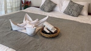 A neatly made bed with a grey bedspread and pillows, a basket with folded towels, and a pair of shoes on the bed. - Baaninkan (Ban Tai)