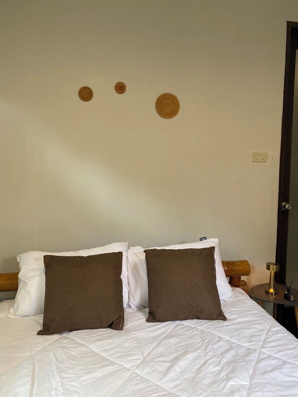 Una cama con ropa de cama blanca y marrón, un cabecero de madera y un adorno circular en la pared.