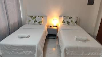 A hotel room with two beds, a nightstand, a lamp, and a window with curtains.