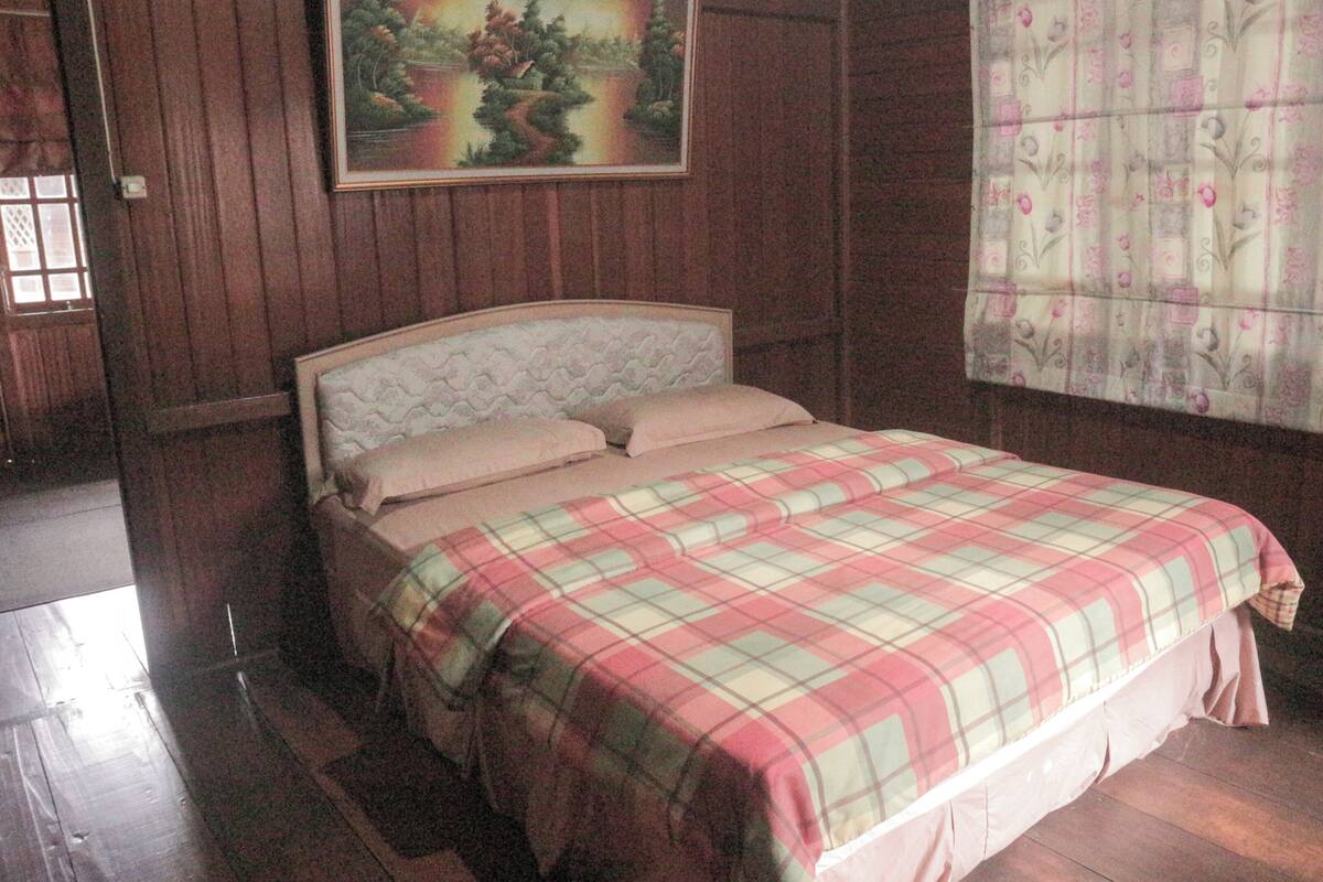 A bedroom with a wooden bed, a plaid bedspread, and a painting on the wall.