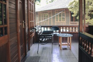 A wooden balcony with a metal bench and a glass table, overlooking a traditional building with wooden windows and a tiled roof. - Jatimas Hijau Hotel & Villa (Cisarua)