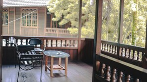 A wooden deck with a glass table and chairs, a railing, and a view of a building and trees. - Jatimas Hijau Hotel & Villa (Cisarua)