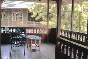 A wooden deck with a glass table and chairs, a railing, and a view of a building and trees. - Jatimas Hijau Hotel & Villa (Cisarua)