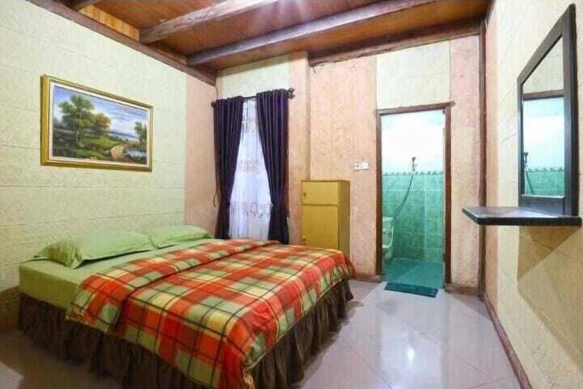 A bedroom with a bed, a painting, a window with curtains, and a door leading to a balcony.