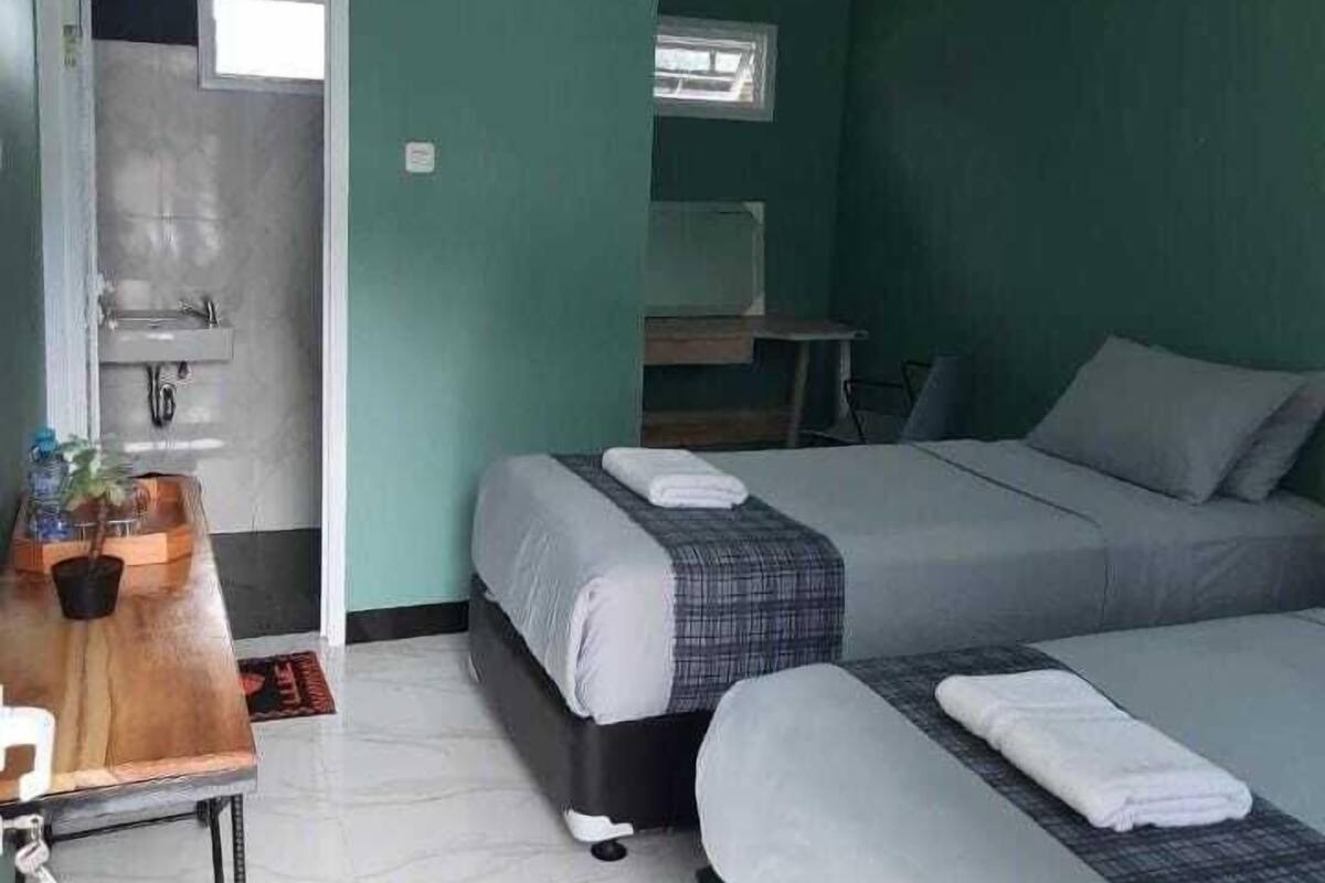 A room with two beds, a small table with a plant, a window, and a door leading to a bathroom.