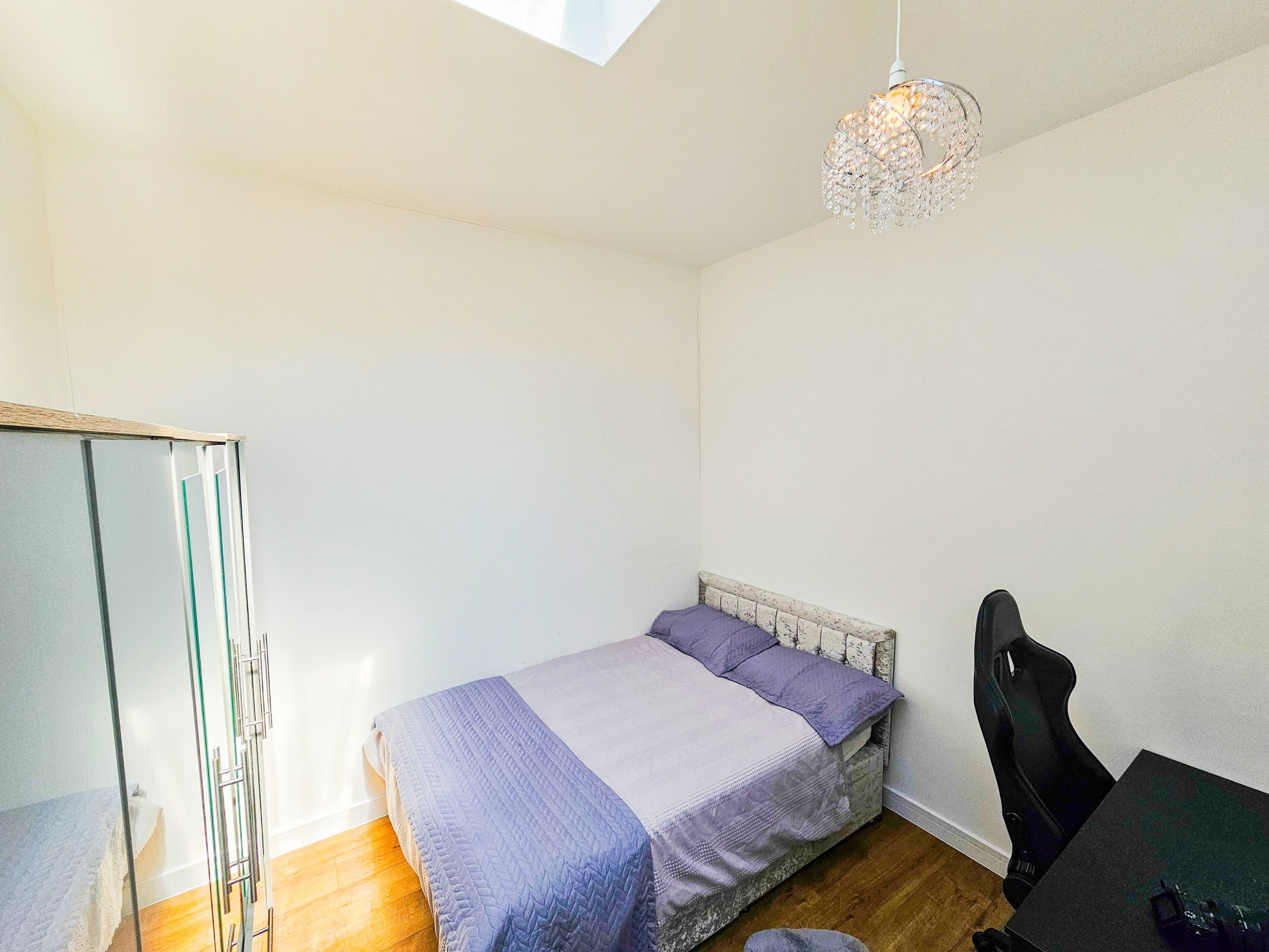 Une petite chambre bien éclairée, avec un lit, un bureau et une chaise.