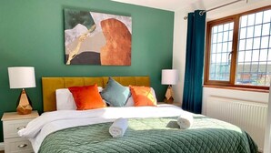 A neatly made bed with a green quilt, multiple pillows, and a rolled towel. - Wakefield 3 Bed Home (West Yorkshire)