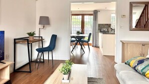 A modern living room with a sofa, a coffee table, and a TV. There is a dining area with a table and chairs, and a kitchen in the background. - Wakefield 3 Bed Home (West Yorkshire)