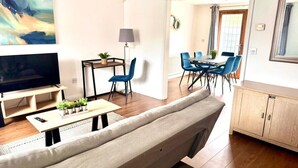 A modern living room with a sofa, TV, and a dining area with blue chairs. - Wakefield 3 Bed Home (West Yorkshire)