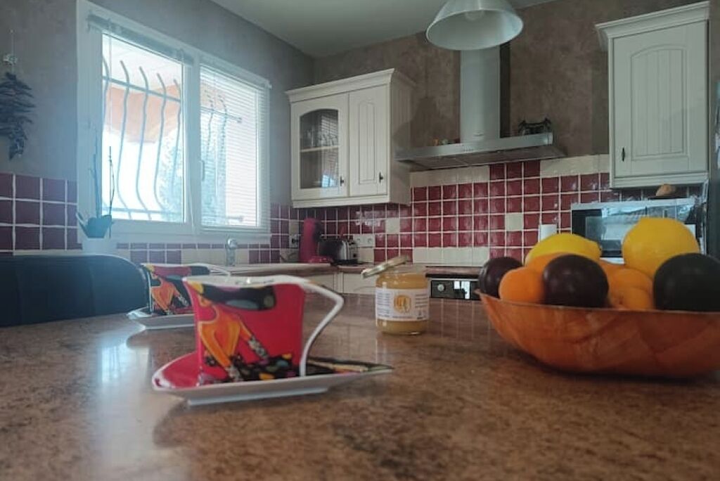 A kitchen with white cabinets, a red tiled backsplash, a fruit bowl on the counter, and a window with bars.