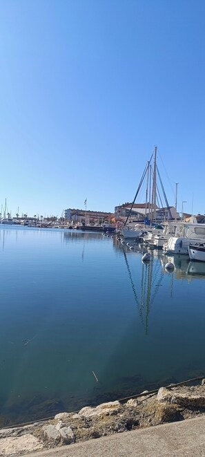 A marina with boats docked, calm water, and a bridge in the background.