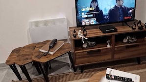 A living room with a television displaying 'The Gentlemen' on Netflix, a wooden coffee table with a remote control, a book, and decorative items. - Home Away From Home (Brierley Hill)